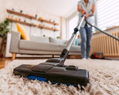 Beautiful senior woman vacuuming the carpet in her apartment. Close-up